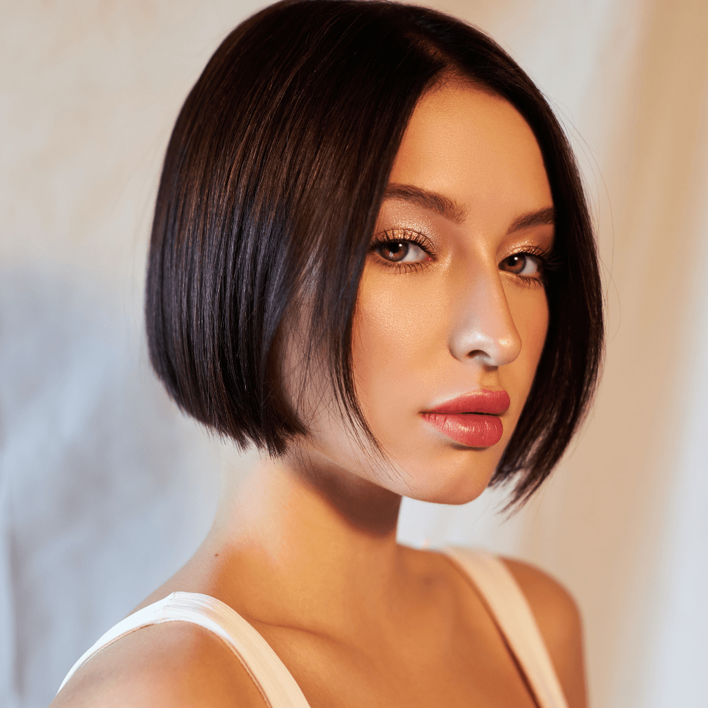 Woman with a sleek, glossy dark bob haircut and flawless makeup, wearing a white top. Styled at Nicolas Ablitt Hair Studio in Corringham, Essex – experts in precision cutting and professional hair colouring for women who want a polished, modern look.